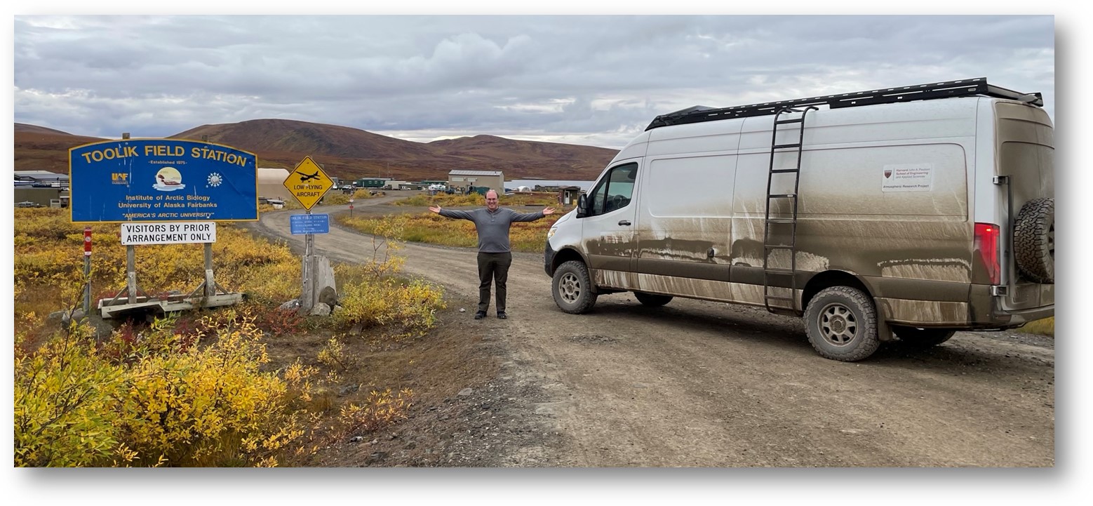 Person standing in front of a field station sign and van